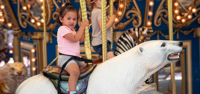 A little girl riding a large polar bear figure on a carousel.