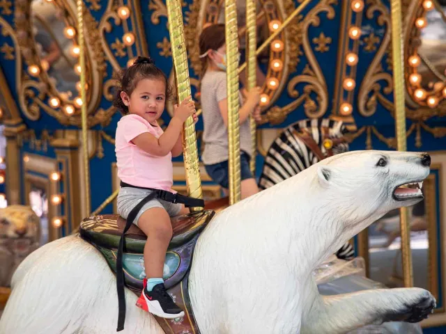 A little girl riding a polar bear on a carousel.