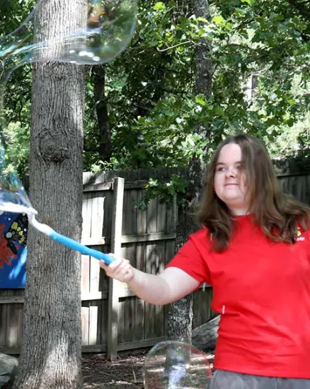 Play Pal teen volunteer moving a bubble wand with a large bubble coming out