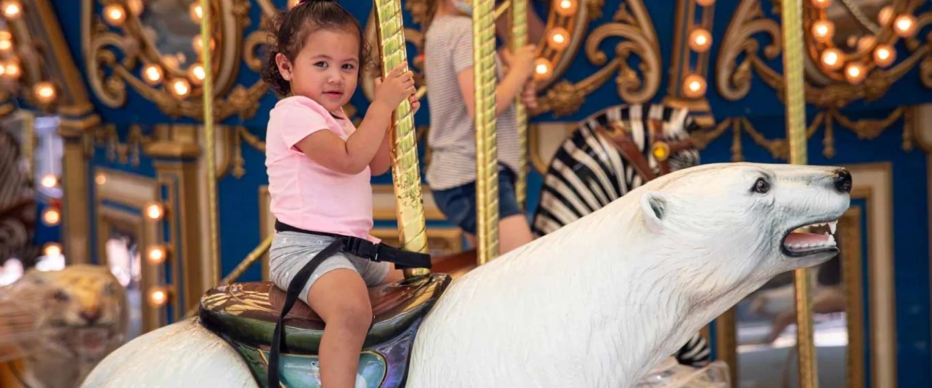 A little girl riding a large polar bear figure on a carousel.