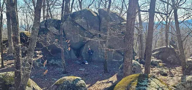 A hiker standing next to an enormous rock on the ridgeline of Ridge's Mountain.