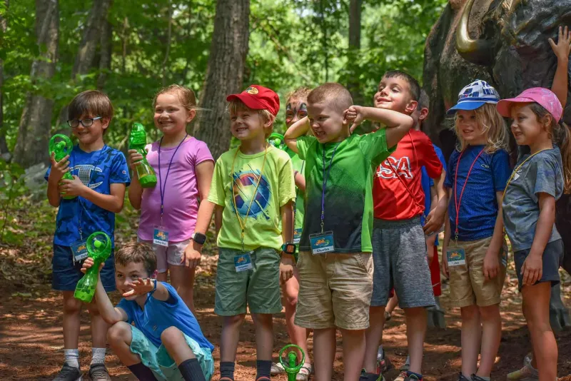 A group of children posing in front of a life-sized bison sculpture attending summer camp.